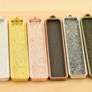 May include: Six metal rectangular pendant trays with a textured surface. The trays are in silver, gold, rose gold, copper, gunmetal, and bronze.