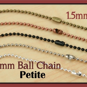 May include: Four different colored 1.5mm ball chains. The chains are silver, black, copper, and antique gold. The chains are all laid out horizontally on a wooden surface. The text "1.5mm Ball Chain Petite" is written below the chains.