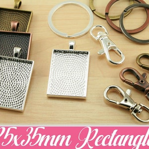 May include: Silver, black, and bronze metal rectangular pendant trays with a textured surface. The trays are 25x35mm and come with a variety of silver, bronze, and black metal keychains and clasps.
