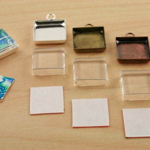 May include: Assortment of square glass and metal pendant trays, some with adhesive backing, and a patterned fabric square.