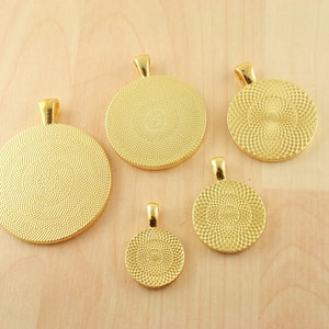 May include: Five gold-colored metal round pendant trays with a textured surface. The trays are different sizes and have a loop at the top for hanging.