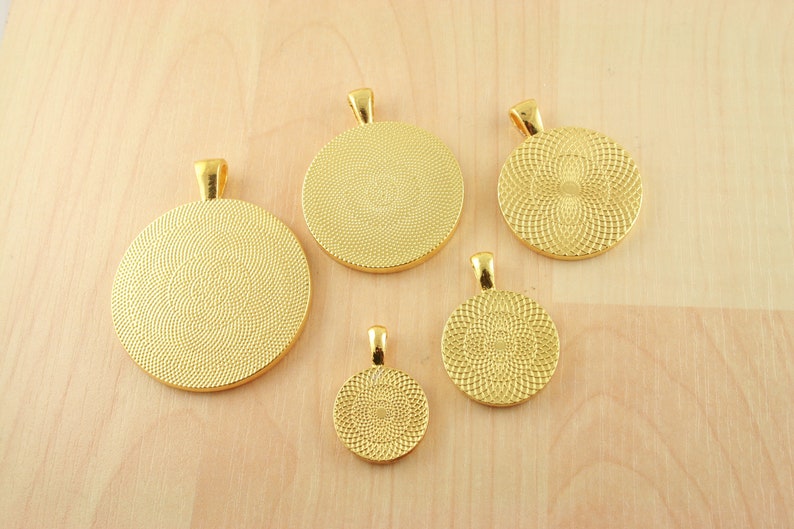 May include: Five gold-colored metal round pendant trays with a textured surface. The trays are different sizes and have a loop at the top for hanging.