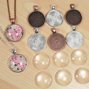 Pode incluir: Conjunto de caboch&otilde;es redondos de vidro em branco e com padr&otilde;es, com engastes de prata e cobre. Os caboch&otilde;es est&atilde;o dispostos sobre uma superf&iacute;cie de madeira. Alguns dos caboch&otilde;es est&atilde;o pendurados em correntes.