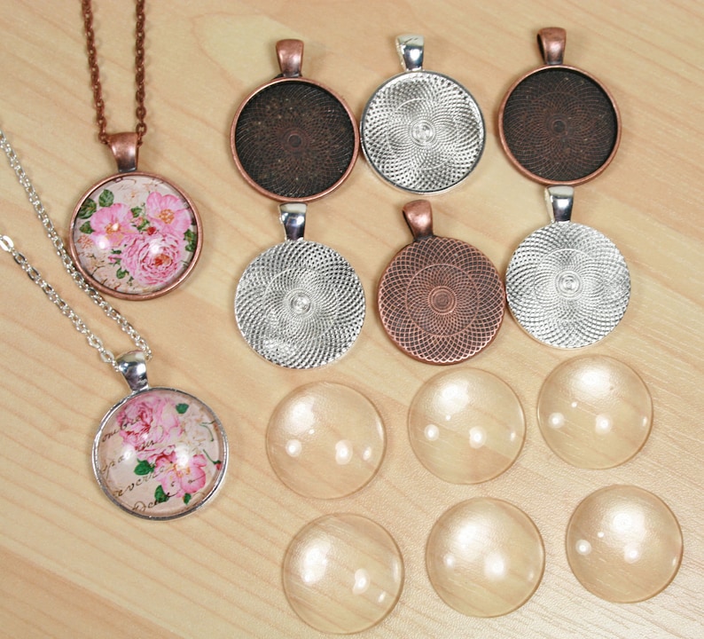 Pode incluir: Conjunto de caboch&otilde;es redondos de vidro em branco e com padr&otilde;es, com engastes de prata e cobre. Os caboch&otilde;es est&atilde;o dispostos sobre uma superf&iacute;cie de madeira. Alguns dos caboch&otilde;es est&atilde;o pendurados em correntes.