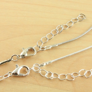 May include: Two silver chains with clasps. One chain is a delicate snake chain and the other is a curb chain.