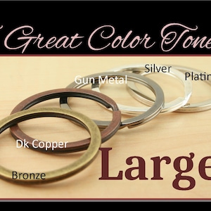 May include: Five large key rings in different metal finishes: bronze, dark copper, gun metal, silver, and platinum. The key rings are arranged in a row on a light wood surface. The text "Large" is written in large, dark red letters below the key rings.