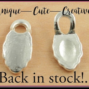 May include: Two silver-toned metal jewelry findings with a loop at the top and a rounded, slightly oval-shaped base. The findings are unique, cute, and creative.
