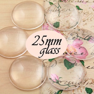 Pode incluir: Cinco caboch&otilde;es de vidro transparente, cada um com um di&acirc;metro de 25 mm, est&atilde;o dispostos sobre uma superf&iacute;cie estampada. Os caboch&otilde;es s&atilde;o redondos e t&ecirc;m um acabamento liso e polido.