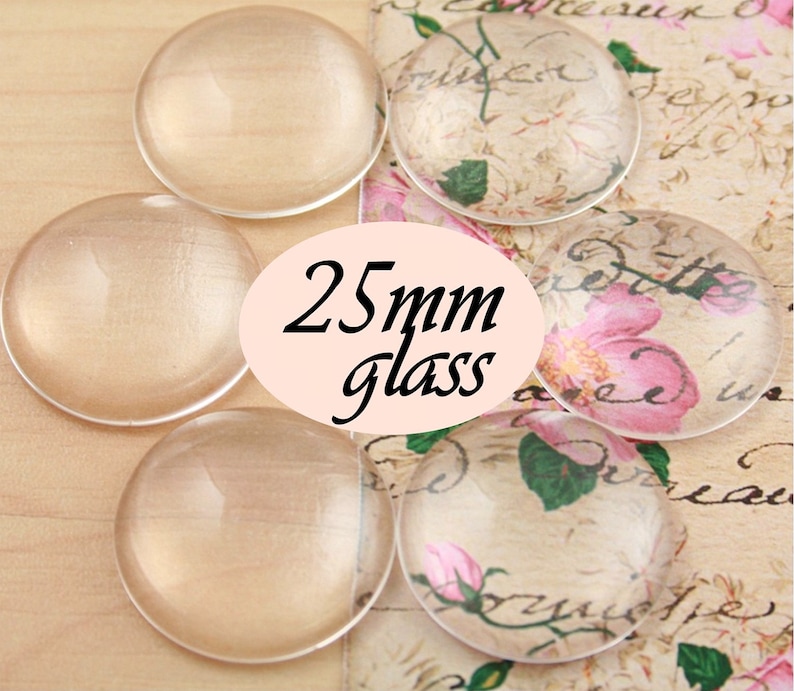 Pode incluir: Cinco caboch&otilde;es de vidro transparente, cada um com um di&acirc;metro de 25 mm, est&atilde;o dispostos sobre uma superf&iacute;cie estampada. Os caboch&otilde;es s&atilde;o redondos e t&ecirc;m um acabamento liso e polido.