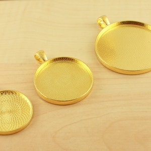 May include: Three gold-toned metal pendant trays with a textured surface. The trays are round and have a loop at the top for hanging.