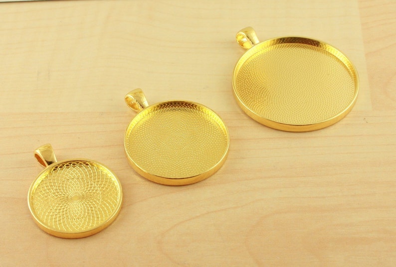 May include: Three gold-toned metal pendant trays with a textured surface. The trays are round and have a loop at the top for hanging.