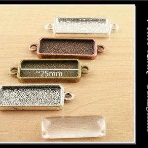 May include: Four silver-toned, copper-toned, and gold-toned metal rectangular frames with rounded corners and two loops on each side. The frames are arranged vertically, with the largest frame at the bottom. A clear glass rectangle is in the foreground. The text "Petite Link - 11x25mm" is visible on the right side of the image.