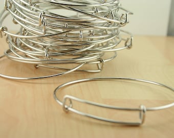May include: A stack of silver bangle bracelets with a single bracelet lying on a wooden surface.