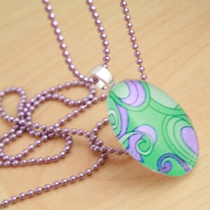 May include: A silver chain necklace with a green and purple oval pendant featuring a swirling abstract design.