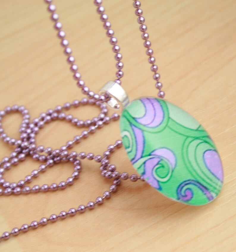 May include: A silver chain necklace with a green and purple oval pendant featuring a swirling abstract design.