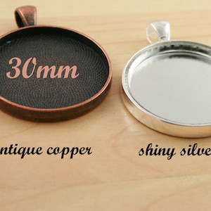 Könnte beinhalten: Zwei runde Metall-Anhänger-Tabletts, eines in Antikkupfer und eines in glänzendem Silber. Beide Tabletts haben einen Durchmesser von 30 mm und eine glatte, ebene Oberfläche.