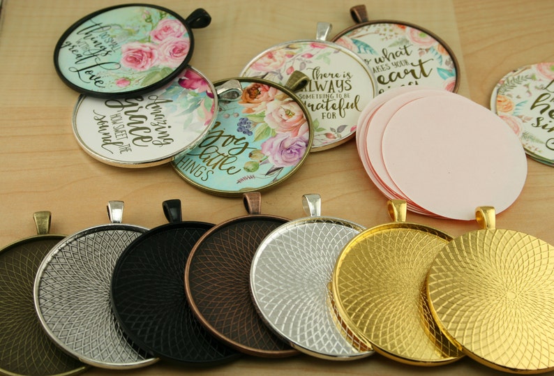May include: Assortment of round metal pendant trays with a variety of finishes, including silver, black, copper, and gold. The trays have a decorative swirl pattern and are ready to be used for crafting projects.  Some of the trays have pre-made designs with floral patterns and inspirational quotes, such as "Amazing Grace" and "There is always something to be grateful for".