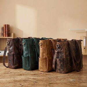May include: Four rectangular leather tote bags arranged in a row, featuring dark brown, forest green, tan, and distressed brown colors. Each bag includes dual top handles, a detachable shoulder strap with metal clips, and a zippered front pocket.