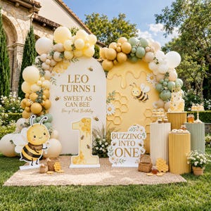 Op de afbeelding: Een feestdecoratie voor een eerste verjaardag met bijenthema, bestaande uit twee boogvormige achtergronden, een witte met de tekst Leo Turns 1 Sweet As Can Bee en een gele met honingraatpatronen. Inclusief ballonslingers en bijenillustraties.