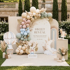 Pode incluir: Um cenário para festa de revelação de gênero com um arco de balões bege, rosa, azul e verde sálvia, capim dos pampas e uma placa com os dizeres SWEET REVEAL OUR SWEET LITTLE SECRET WILL SOON BE REVEALED HE OR SHE? com ponto de interrogação.
