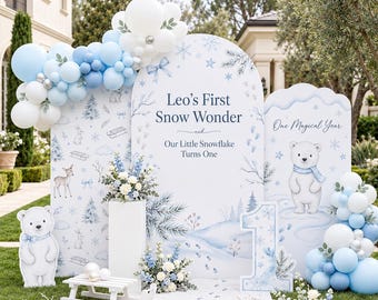 May include: A birthday party backdrop set featuring white and light blue balloons, a large arched sign with the text Leo's First Snow Wonder, a smaller sign with a polar bear, and a number one cutout, all decorated with winter motifs.