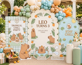 May include: A party decoration set featuring capybara illustrations, orange accents, and tropical foliage. The signs display text including 'LEO TURNS 3', 'TROPICAL CHILL PARTY', 'STAY CHILL', and 'CHILLIN' INTO THREE', accompanied by a balloon arch and pedestals.