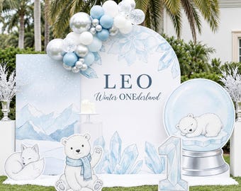 May include: A party backdrop set featuring a large arched sign with the text LEO and Winter ONEderland, decorated with a blue, white, and silver balloon garland, a polar bear cutout, a fox cutout, a snow globe cutout, and a number one sign.
