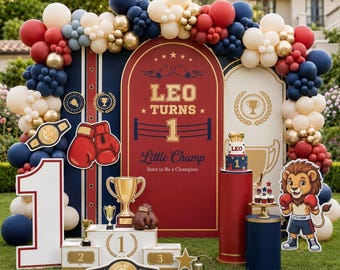 May include: A boxing-themed party backdrop featuring a red and blue arch with the text 'LEO TURNS 1', a lion mascot, a gold trophy, a winner's podium, boxing gloves, and a championship belt, all framed by a large balloon garland in red, blue, and cream.