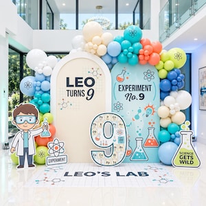 Può includere: Uno sfondo per feste a tema scientifico con due pannelli ad arco, beige e azzurro, con la scritta LEO TURNS 9 ed EXPERIMENT No. 9. Un grande ritaglio del numero 9 con design della tavola periodica, archi di palloncini e un tappetino LEO'S LAB.