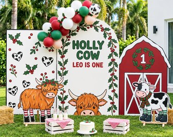 May include: A party backdrop set featuring a white arch with the text HOLLY COW LEO IS ONE, a rectangular panel with holly and cow print hearts, and a red barn panel with a number 1 wreath. Includes two cow illustrations and a cake.