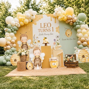 Peut inclure: Un décor de fête d'anniversaire sur le thème des abeilles avec des ballons jaunes, vert sauge et blancs. Le panneau central indique LEO TURNS 1 Little Honey Bee, avec des illustrations d'abeilles, de ruches et un pot de miel. Un grand chiffre 1.