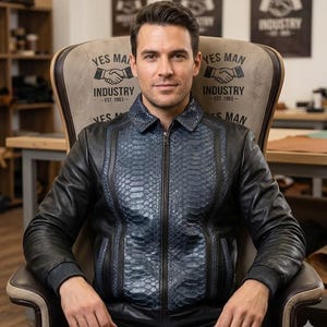 May include: A black leather jacket with a blue snakeskin-effect panel on the front. The jacket features a zip closure and ribbed cuffs. The chair behind the jacket has the text "YES MAN INDUSTRY - EST. 1953-" printed on it.