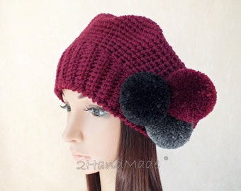 May include: A burgundy knitted beanie with three pom-poms: one black, one gray, and one burgundy. The beanie is crocheted and has a simple design.