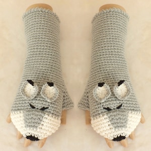May include: A pair of gray fingerless gloves with white and black wolf faces. The gloves are crocheted and have a textured surface.