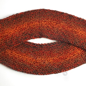 Pode incluir: Uma echarpe infinita de malha em tons de marrom, laranja e vermelho. A echarpe é feita com um fio texturizado e tem um brilho sutil.