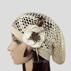 Peut inclure: Un chapeau crocheté beige avec une grande fleur crocheté blanche et des accents de ruban brun. Le chapeau est fait avec un motif ajouré délicat.