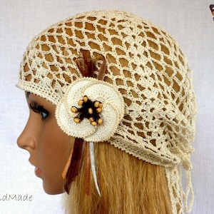 May include: A crocheted cream-colored hat with a flower embellishment and brown feathers. The hat has a long tie that can be tied in the back.