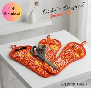May include: Two fabric scissors cases featuring an orange, yellow, and white floral pattern with orange trim and hanging loops. A pair of grey scissors is placed inside one case. Text reads: Ordia's Original Scissors Case, PDF Download, Included: 3 sizes.