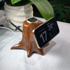 May include: A wooden phone and watch charging station in the shape of a tree stump. A silver iPhone displays the date and time, while a silver Apple Watch rests on top. A black decorative sword is inserted into the side.