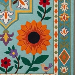 May include: A light blue area rug featuring a large central orange sunflower, smaller red and purple flowers, and green leaves. The design includes a stylized deer, a small bird, and a geometric border with orange diamonds and floral motifs.