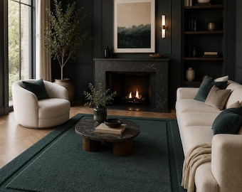 May include: A dark green area rug with a textured surface and a border design, placed in a living room with a cream-colored sofa, a matching cream-colored armchair, a round dark stone coffee table, and a fireplace with a black marble surround.