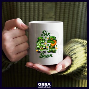May include: White ceramic mug featuring a St. Patrick's Day design. The mug displays the words "Six Seven" with a green number six and a leprechaun figure. The design includes shamrocks and gold coins. The mug is held by a person.