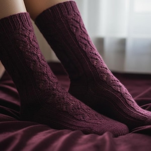 Puede incluir: Un par de calcetines de punto color burdeos con un diseño de trenzas. Los calcetines son hasta la rodilla y tienen un puño acanalado. Los calcetines se muestran sobre una superficie burdeos.