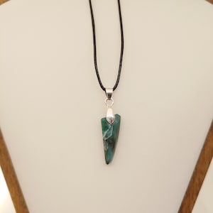 May include: A green gemstone pendant necklace. The pendant is a triangular shape with a silver-coloured metal cap and a black cord. The gemstone has a marbled appearance with shades of green and black.