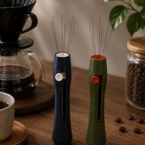 Puede incluir: Dos herramientas de distribución de café con finas agujas metálicas que sobresalen por la parte superior. Una herramienta tiene un mango azul oscuro con un botón deslizante blanco y la otra un mango verde oliva con un botón naranja, ambas verticales.
