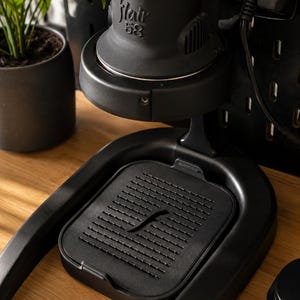 May include: A black Flair 58 manual espresso maker featuring a cylindrical brew head with the Flair 58 logo embossed on the front, a rectangular drip tray with a slotted surface, and a sturdy base structure with a matte finish and metallic accents.