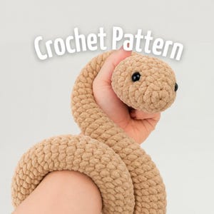 Könnte beinhalten: Ein beigefarbenes Häkelschlange-Stofftier mit einer texturierten, geschlungenen Garnoberfläche und zwei kleinen schwarzen Perlenaugen. Der Text "Crochet Pattern" steht in weißen Buchstaben über der kreisförmig gewundenen Schlange.