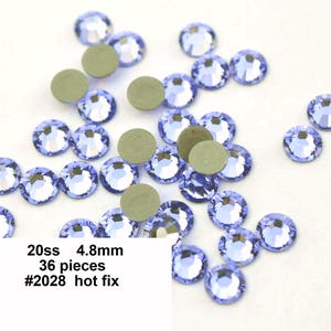 May include: A close-up of 36 light blue, 4.8 mm hot fix rhinestones. The rhinestones are scattered on a white surface. 20ss #2028 hot fix.