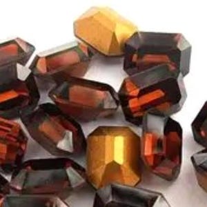 May include: A collection of faceted glass beads in shades of brown, orange, and gold. The beads are all different shapes and sizes, and they have a shiny, iridescent finish.