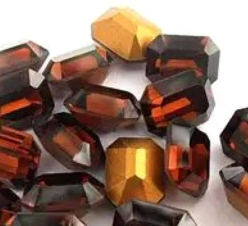 May include: A collection of faceted glass beads in shades of brown, orange, and gold. The beads are all different shapes and sizes, and they have a shiny, iridescent finish.